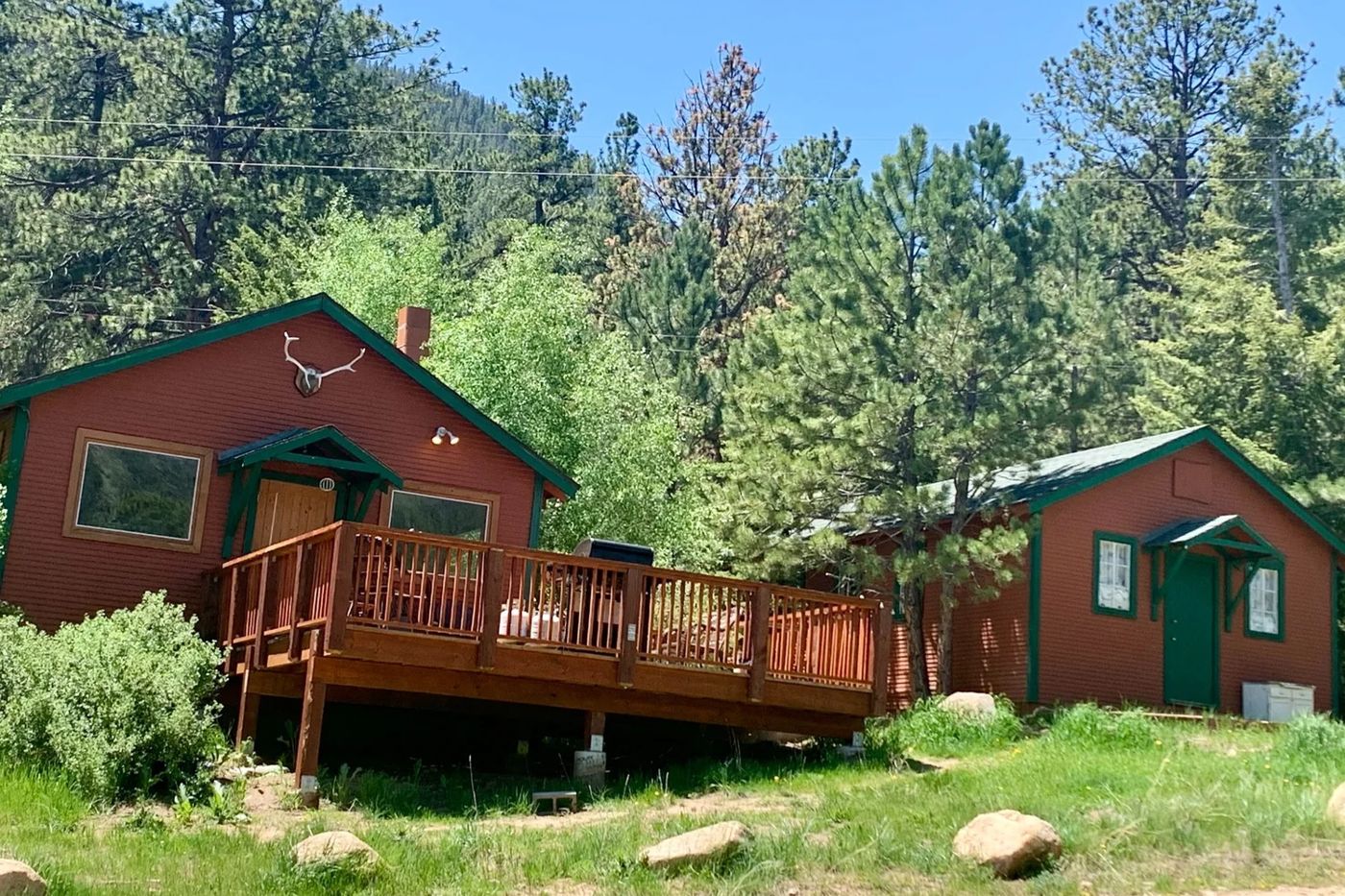 Red-trimmed Refuge cabins with a deck among pine trees